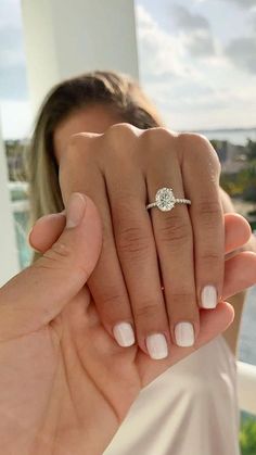 a woman's hand with a ring on her finger and the other hand holding an engagement ring