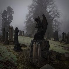 an angel statue sitting on top of a rock in the middle of a cemetery filled with tombstones