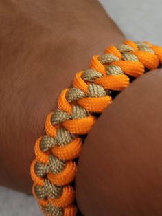 an orange and gold bracelet on someone's arm with two braids attached to it