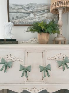 a white dresser with green bows on the drawers and a painting in the corner behind it