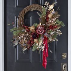 a wreath on the front door decorated with red and gold flowers, leaves and berries