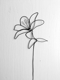 a metal flower on a white wall with black wire hanging from it's center