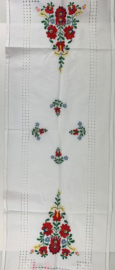 an embroidered white cloth with red flowers and green leaves on the border, hanging from a wall