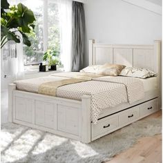 a white bed with drawers underneath it in a room next to a window and rug