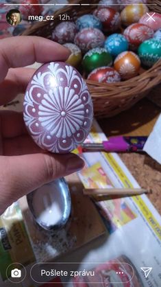 someone is holding an easter egg in front of some other eggs on the table with paintbrushes