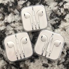 three earphones are sitting in a case on a marble counter top, one is white and the other is silver