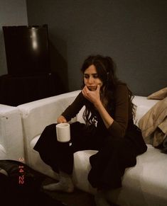 a woman sitting on top of a white couch holding a coffee cup in her hand