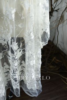 white sheer lace fabric with flowers and leaves on the bottom, in front of a wooden floor