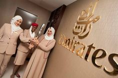 two women in hijabs are standing next to a wall with the name emirates on it