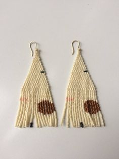 two white and brown beaded earrings are hanging from hooks on a white tablecloth