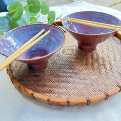 two bowls with chopsticks in them sitting on a table next to some plants