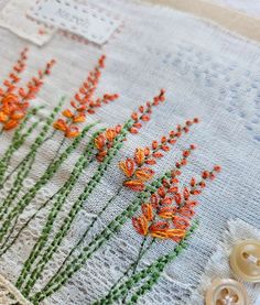 an embroidered piece with orange flowers and green stems on the side, next to buttons