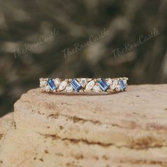 a diamond and blue topazte band ring sitting on a piece of rock in front of some trees