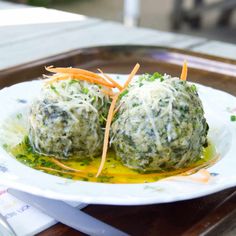 two balls of broccoli and cheese are on a white plate with carrots