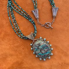 "- A handcrafted, locally sourced, one of a kind, statement necklace. - Chrysocolla is a semi-precious gemstone found in Arizona.  This one was cut and polished by a local rock hound. I bought the cabochon from him at an outdoor Boutique market in our town.  I used silver plated 20 and 26  gauge wire to weave the pendant and bail. I added 13 glass pearls around the edge of the pendant.  I used the same wire plus a small medallion on the back to secure and decorate it.    - The 21\" necklace is m Artisan Amazonite Beaded Jewelry, Elegant Handmade Turquoise Chrysocolla Necklace, Artisan Beaded Amazonite Jewelry, Artisan Wire Wrapped Chrysocolla Jewelry, Handmade Earthy Turquoise Necklace For Gift, Turquoise Jasper Round Bead Jewelry, Unique Wire Wrapped Turquoise Pendant Necklace, Unique Wire-wrapped Turquoise Pendant Necklace, Artisan Necklace With Amazonite Gemstone Beads