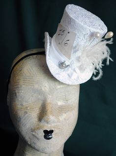 A Mad Hatter mini top hat with a bridal twist! The hat is covered with beautiful textured white brocade and embellished with white taffeta ribbon around the crown. Trimmed with pearl hats pins, white roses,white feather spray, the signature 10/6 Mad Hatter card and of course a tiny silver tea-pot! Cause around here it's always tea-time! Both hat pins have push-in clasps to avoid accidents! IMPORTANT NOTE: The fabric used in the original design is permanently OUT OF STOCK. Please check out the NE Vintage Top Hat With Curved Brim For Costume Party, Vintage Curved Brim Top Hat For Costume Party, Vintage Fitted Costume Hats And Headpieces For Carnival, Vintage Fitted Costume Hats For Carnival, White Fitted Mini Hats For Vintage Events, Vintage Costume Hats And Headpieces For Wedding Carnival, Whimsical Fitted Top Hat With Short Brim, Fitted Mini Hats For Wedding And Carnival, Adjustable Top Hat For Wedding And Carnival