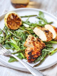 a white plate topped with chicken, asparagus and lemon wedges next to a fork