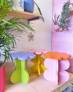 three colorful stools sitting on top of a wooden table next to a potted plant