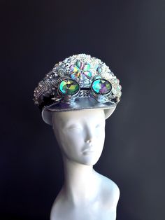 The hat is encrusted with iridescent crystals and sequins that catch the light and reflect a spectrum of colors, ensuring you stand out in any crowd. The silver spike goggles provide a striking contrast to the shimmering crystals, creating a perfect blend of elegance and rebellion. Age Group/Gender - Adult/Women Size/Type - One size fits all adults Color - Silver Special Features - Silver spike goggles Adjustable Rhinestone Festival Headpiece, Adjustable Festival Headpiece With Rhinestones, Adjustable Rhinestone Headpiece For Festival, Silver Tall Crown Headpiece For Party, Adjustable Silver Headpiece For Carnival, Silver Adjustable Headpieces For Carnival, Silver Headpiece With Structured Crown For Party, Silver Structured Crown Headpieces For Party, Adjustable Silver Party Hat