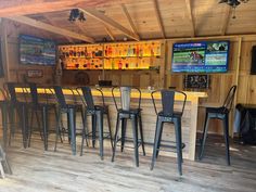 a bar with several stools in front of it and television screens on the wall