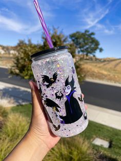 a hand holding a glittered cup with a purple straw in it and two bats on the top