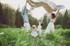 two adults and three children are playing in the grass with a blanket over their heads