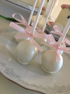 three white cake pops with pink bows on them sitting on a plate in front of a mirror