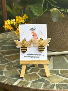 a pair of bee earrings sitting on top of a table next to a potted plant