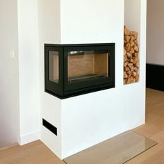 a fireplace with wood stacked on top of it in a room that has white walls and wooden floors