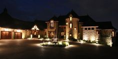 a large house with lots of lights on it's front yard and driveway at night