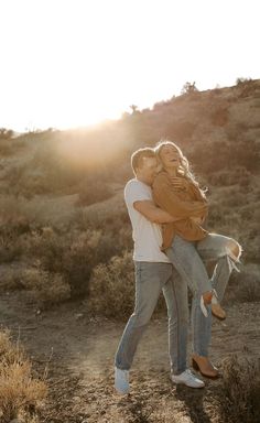 a man carrying a woman on his back in the middle of a desert field at sunset