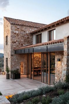 the outside of a stone house with glass doors and an outdoor dining area in front