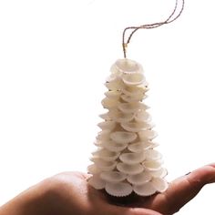 a hand holding a small christmas tree made out of seashells on a string