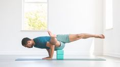 a man is doing a yoga pose on a blue mat in front of a window