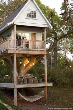 a tree house with a hammock in the front yard and deck on top