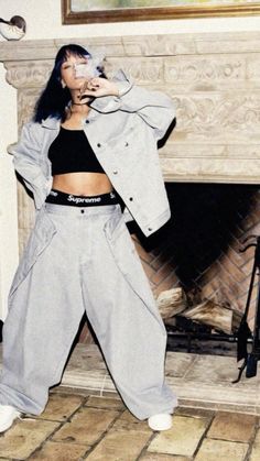 a woman standing in front of a fire place wearing grey sweatpants and a jacket