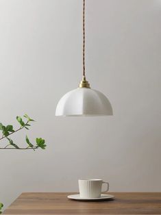 a white cup sitting on top of a wooden table next to a light hanging over it