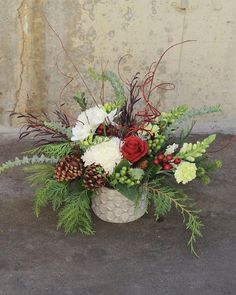 a vase filled with flowers and greenery on top of a cement floor next to a wall