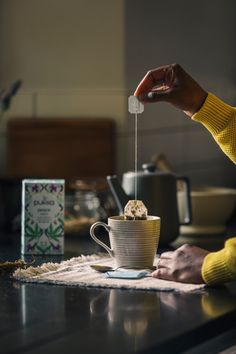 a person pouring something into a cup on top of a table next to a tea bag