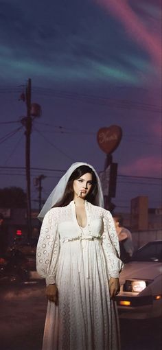 a woman in a white dress and veil standing on the side of a road at night