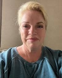 a woman with blonde hair wearing a blue shirt and looking at the camera while sitting in front of a mirror