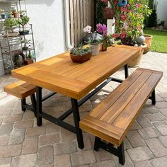 a wooden table with two benches next to potted plants on the side of it