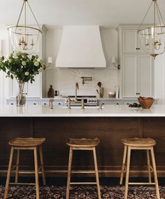 three wooden stools sit in front of an island with white cabinets and counter tops