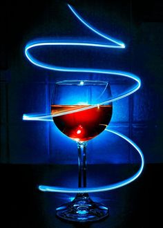 a glass of red wine sitting on top of a table next to a neon light