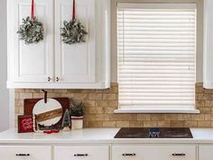 a kitchen with white cabinets and christmas wreaths on the window sill above the stove