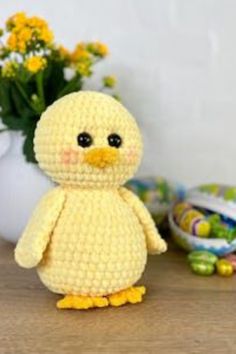 a crocheted yellow bird sitting on top of a wooden table next to flowers