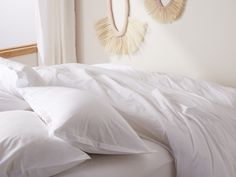 two wall hangings above a bed with white sheets and pillows on the headboard