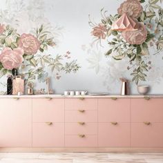 a pink dresser in front of a floral wallpaper with gold handles and knobs