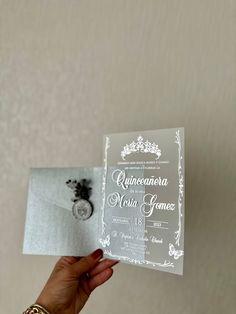 a person holding up a wedding card with a ring on it's finger and an envelope in the other hand