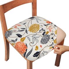 a hand is holding the back of a wooden chair with a flower print seat cover